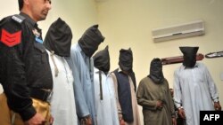 A Pakistani policeman stands guard alongside suspects who allegedly killed Sikh politician Sardar Soran Singh during a press conference after their arrest in Peshawar on April 25.