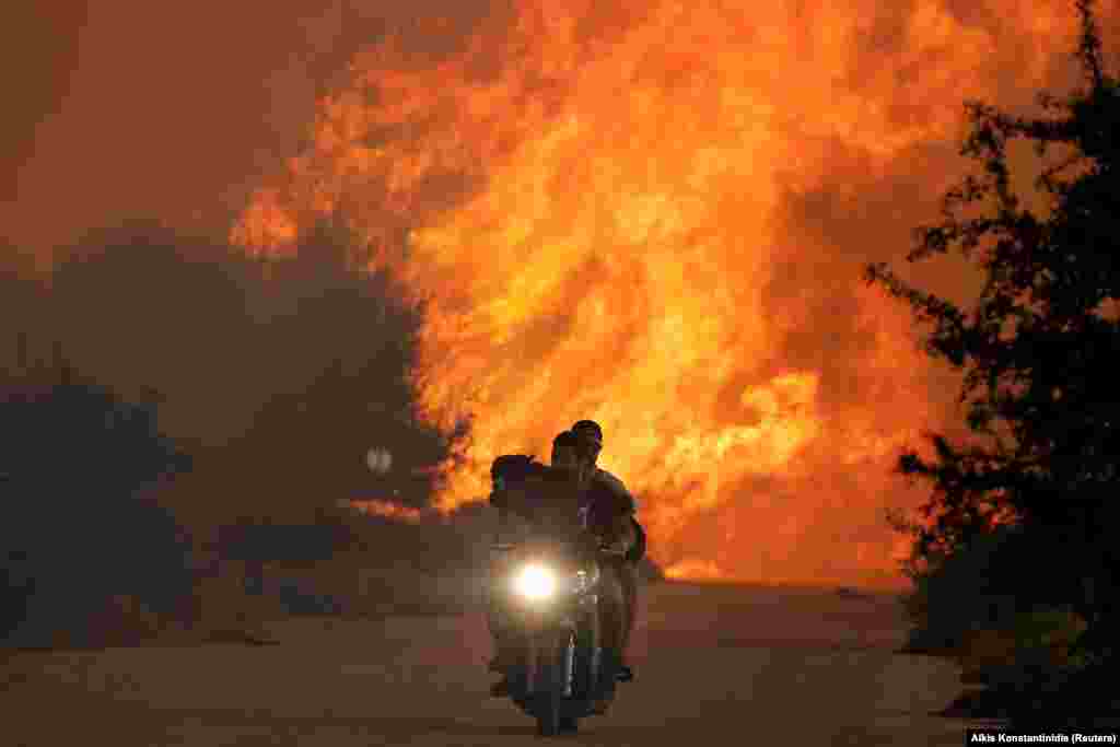 Two men and a dog on a motorbike flee a wildfire burning near the village of Varnavas, north of Athens, on August 14. (Reuters/Alkis Konstantinidis)