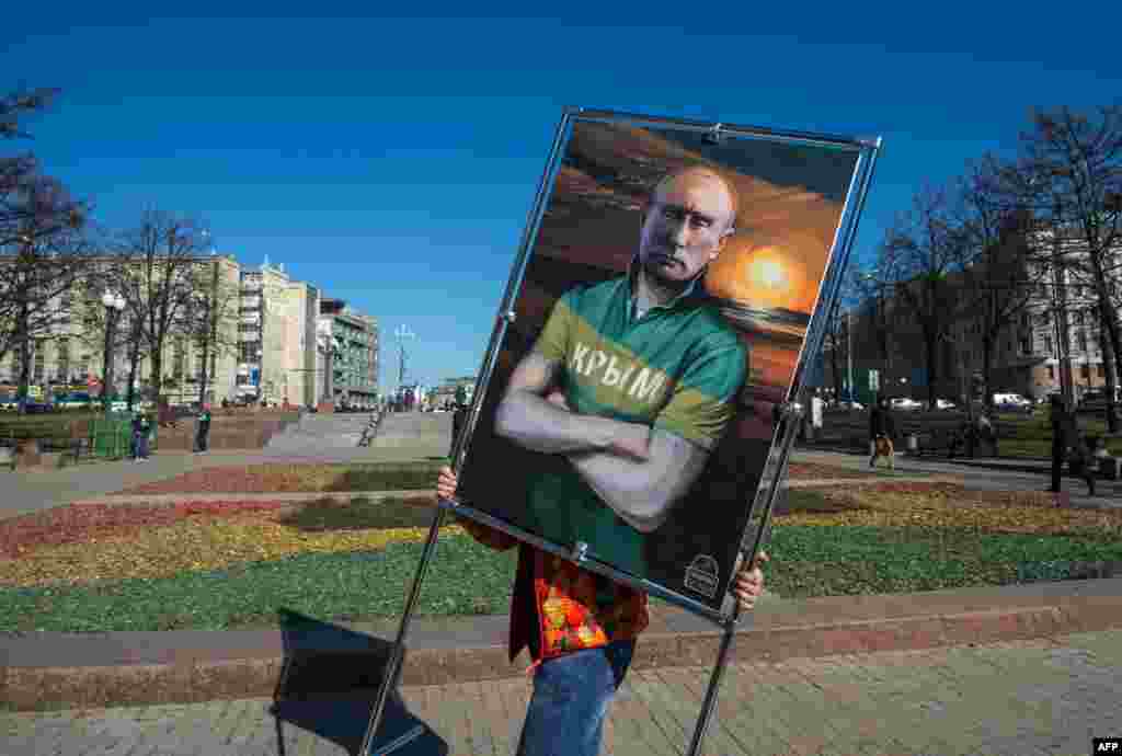 A man carries a picture depicting Russian President Vladimir Putin in a T-shirt with an inscription reading "Crimea" at an open-air political cartoons exhibition in Moscow marking the one-year anniversary of Russia's annexation of the peninsula. The annexation was declared illegal in an overwhelming vote by the UN General Assembly. (AFP/Dmitry Serebryakov)