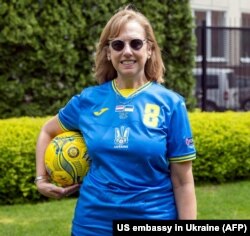 Vezérszurker – a kijevi amerikai nagykövetség ügyvivője, Kristina A. Kvien az ukrán labdarúgó-válogatott mezében. Az UEFA az orosz tiltakozás után levetette a mezről a „Dicsőség Ukrajnának!" szlogent