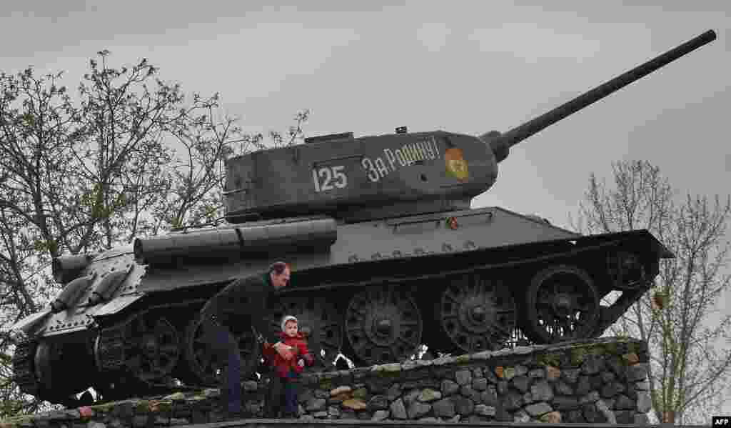 Moldova -- A man and his child are pictured next to a soviet era tank, now a monument celebrating the victory of the Red Army against fascist Germany, in Tiraspol, April 16, 2014