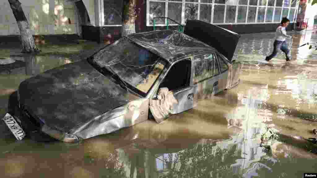 A local resident passes by a damaged car stuck in a flooded street in Krymsk.