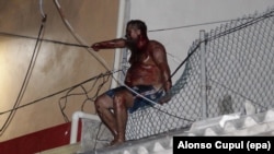 Aleksei Makeyev sits on a fence atop a building while covered in blood after an angry mob tried to lynch him for reportedly insulting Mexican people in Cancun on May 19.