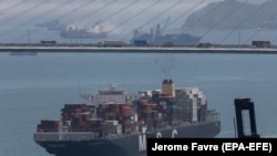 Egy konténerhajó halad át a Kőfaragók hídja alatt a hongkongi Kvaj Csing konténerterminál felé 2019. május 14-én. Képünk illusztráció