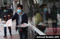 У Гонконгу жінки в захисних масках для обличчя роздають листівки про коронавірус в Ухані