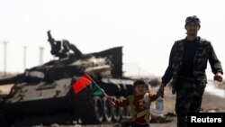 Pobunjenik vodi svog sina dalje od linije fronta blizu grada Ajdžabija, 12. april 2011.