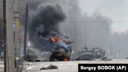 Kilőtt orosz páncélozott csapatszállító jármű (BTR), előtte egy nem azonosított fegyveres holttestével Harkivban 2022. február 27-én