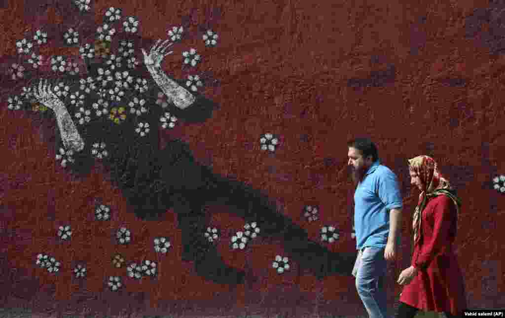 A man and a woman walk past a mural on a sidewalk in downtown Tehran. (AP/Vahid Salemi)