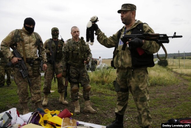 Бойовик російських гібридних сил тримає іграшку, знайдену на місці падіння уламків «Боїнга», збитого російською установкою «Бук», в результаті чого загинуло 298 людей, в тому числі 80 дітей. Донеччина, неподалік села Грабове, 19 липня 2014 року