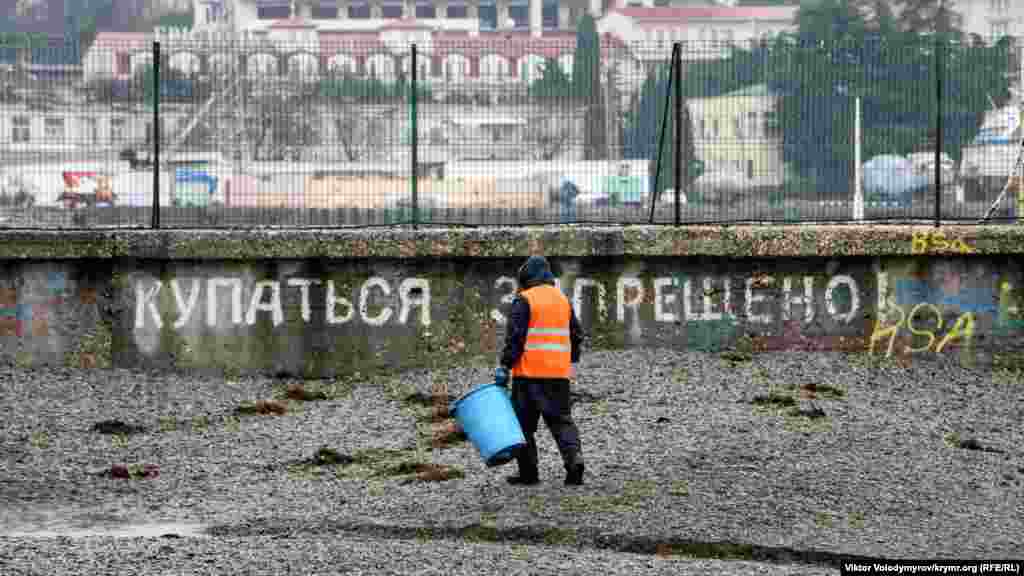 Уборщик собирает водоросли на городском пляже