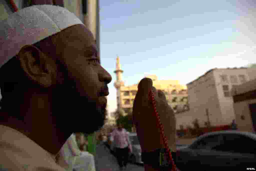 A worker holds prayer beads near a mosque.