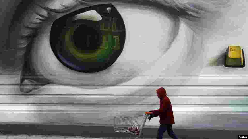 A man pushes an empty shopping trolley past graffiti in a poor Athens neighborhood. (REUTERS/Yannis Behrakis)