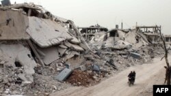 Syrians ride a motorcycle amid the destruction in a neighborhood in the rebel-held area of Daraa in April.