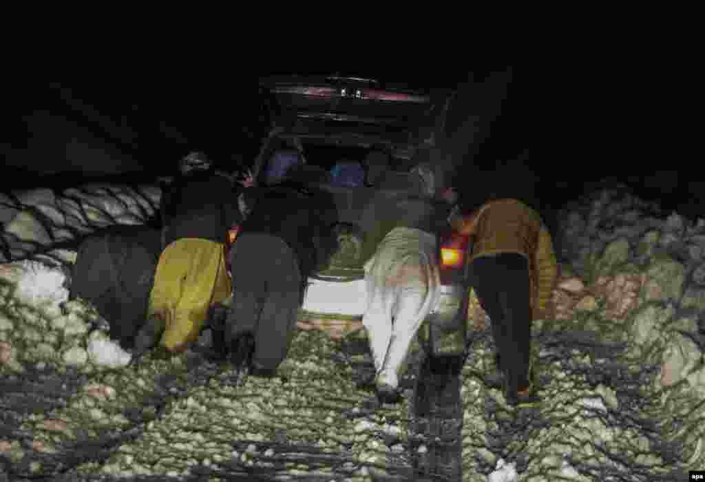 Men push a car through the snow near the site of an avalanche.