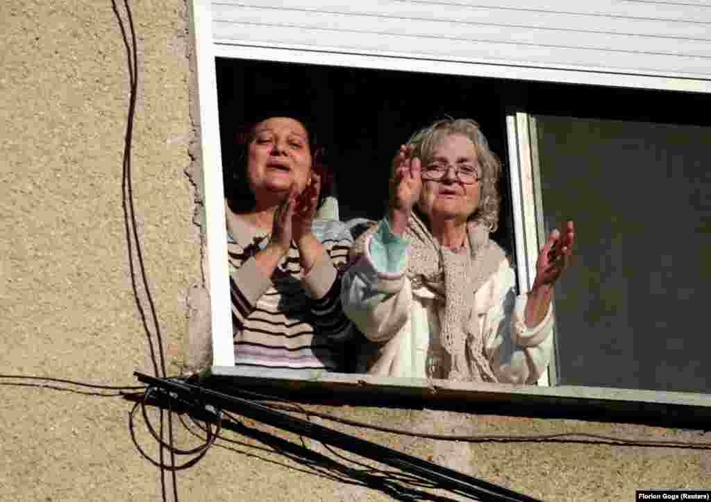 Албанские женщины аплодируют из окна своей квартиры певцу, который их развлекает, распевая во дворе дома, 7 апреля