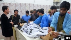 Paramedics, colleagues and other men stand beside the bodies of two policemen who were killed in Quetta on January 28.