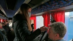 Medicinska radnica s maskom na licu provjerava temperaturu putnika u autobusima koji su prešli granicu u selu Uspenka u Donjecku, 20. marta 2020.