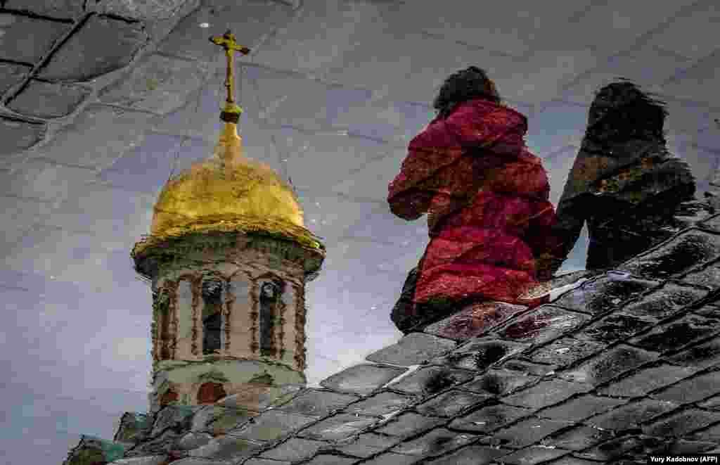 Two women are reflected in a puddle as they walk across Red Square in Moscow on April 26. (AFP/Yuri Kadobnov)