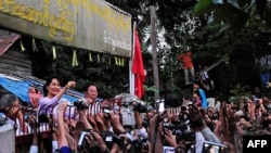 Freed opposition leader Aung San Suu Kyi, left, waves at her cheering supporters from the gate of her house.