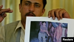 Saddam Saleh, a former prisoner at Abu Ghraib, shows a photograph at a 2004 press conference from the scandal that includes him in the middle of a group of naked prisoners being mocked by Lynndie England.
