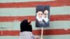 A woman displays the images of Iran Supreme Leader Ali Khamenei and Islamic Republic founder Ruhollah Khomeini outside the wall of the former U.S. Embassy in Tehran.