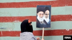 A woman displays the images of Iran Supreme Leader Ali Khamenei and Islamic Republic founder Ruhollah Khomeini outside the wall of the former U.S. Embassy in Tehran.