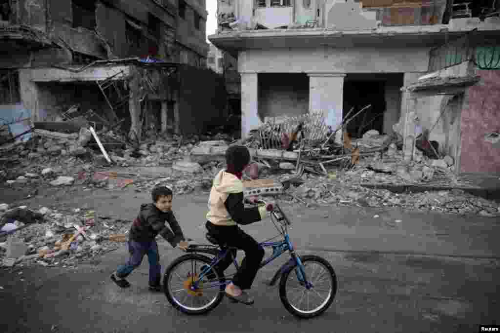 Children play on a bicycle among war-damaged buildings...