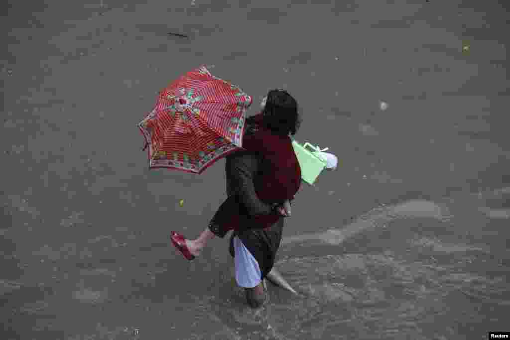 A man carries his daughter as he wades through a flooded road after heavy rains in Lahore.