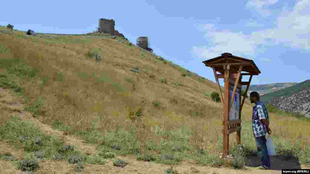 Турист изучает информационный стенд Большой Севастопольской тропы. На холме &ndash; развалины генуэзской крепости Чембало. Отсюда начинается и наш путь
