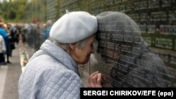 An elderly Russian woman, a granddaughter of a Stalin terror victim, touches her head to a name of her grandfather, written on the memorial wall at Butovo shooting range outside Moscow.