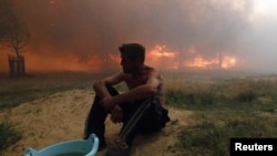 A man sits on the ground while a house burns due to severe heat, outside the western Russian town of Vyksa in July.