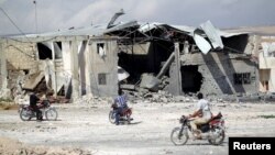 Men on motorcycles inspect a site hit by what activists said were air strikes carried out by the Russian Air Force in the southern town of Babila on October 7.
