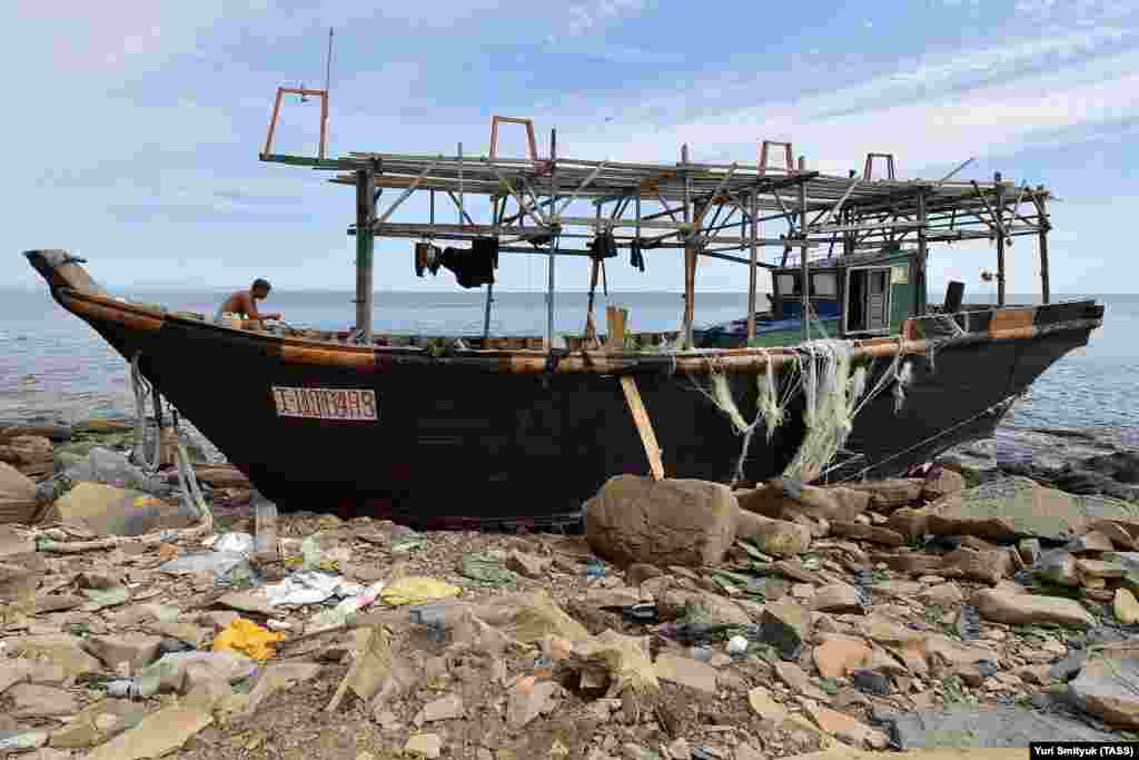 A Russian fisherman sits on his boat after being forced ashore by a storm on Russky Island. (TASS/Yuri Smityak)&nbsp;