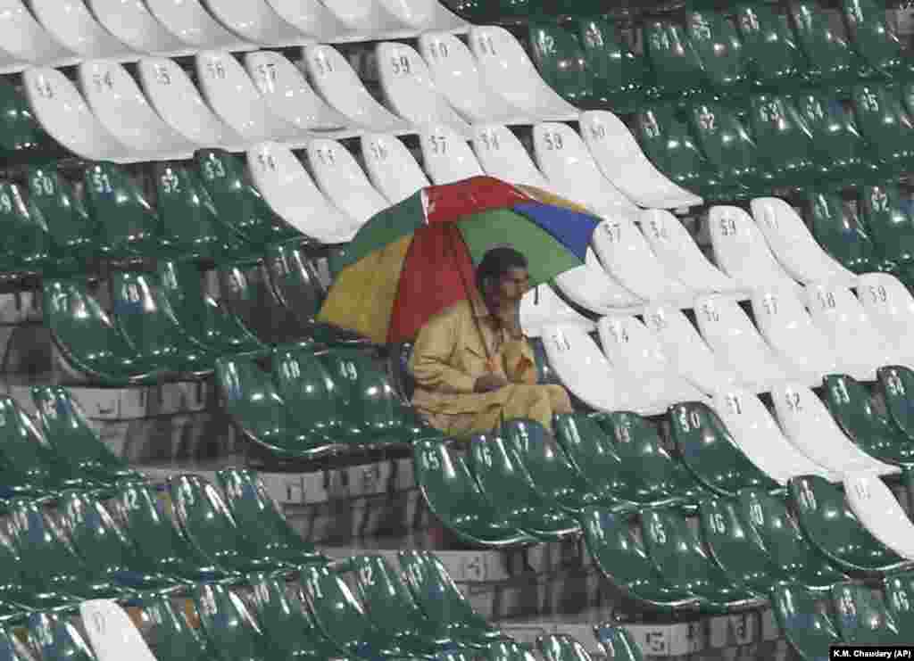 A spectator at Gaddafi Stadium sits alone in the stands with an umbrella as heavy rain falls in Lahore. Pakistan abandoned the Pakistan Super League match between title defender Quetta Gladiators and Multan Sultans on March 11. (AP/K.M. Chaudhry)