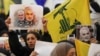 A supporter of the Shiite Hezbollah movement holds a poster of slain Iraqi paramilitary chief Abu Mahdi al-Muhandis (L) and Iranian Major General Qasem Soleimani (R) as the movement's leader delivers a speech on a screen, in the Lebanese capital Beirut. January 5, 2020 