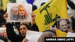 A supporter of the Shiite Hezbollah movement holds a poster of slain Iraqi paramilitary chief Abu Mahdi al-Muhandis (L) and Iranian Major General Qasem Soleimani (R) as the movement's leader delivers a speech on a screen, in the Lebanese capital Beirut. January 5, 2020 