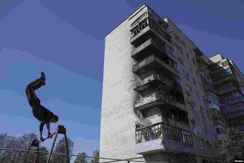 A youth practices on the bars at a park near a building damaged in recent shelling in the town of Ilovaysk in eastern Ukraine. (Reuters/Marko Djurica )