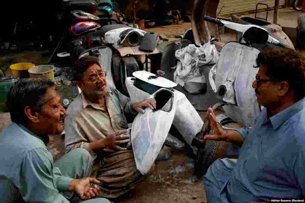 A restorer (center) chats with customers while applying an undercoat to a Vespa panel.