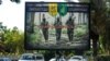 IRAQ -- A picture taken on June 20, 2018 shows a propaganda billboard for the pro-Iran Hezbollah Brigades militia hanging over Palestine Street in the centre of the Iraqi capital Baghdad, depicting three of their masked fighters walking along a road betwe