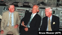Командир "Аполлона-11" Нил Армстронг (слева) и командир "Аполлона-17" Джин Сернан (справа) слушают Эдвина (Базза) Олдрина, отвечающего на вопросы прессы. Копия кабины управления запуска "Аполлона"/"Сатурна-5" в Космическом Центре Кеннеди