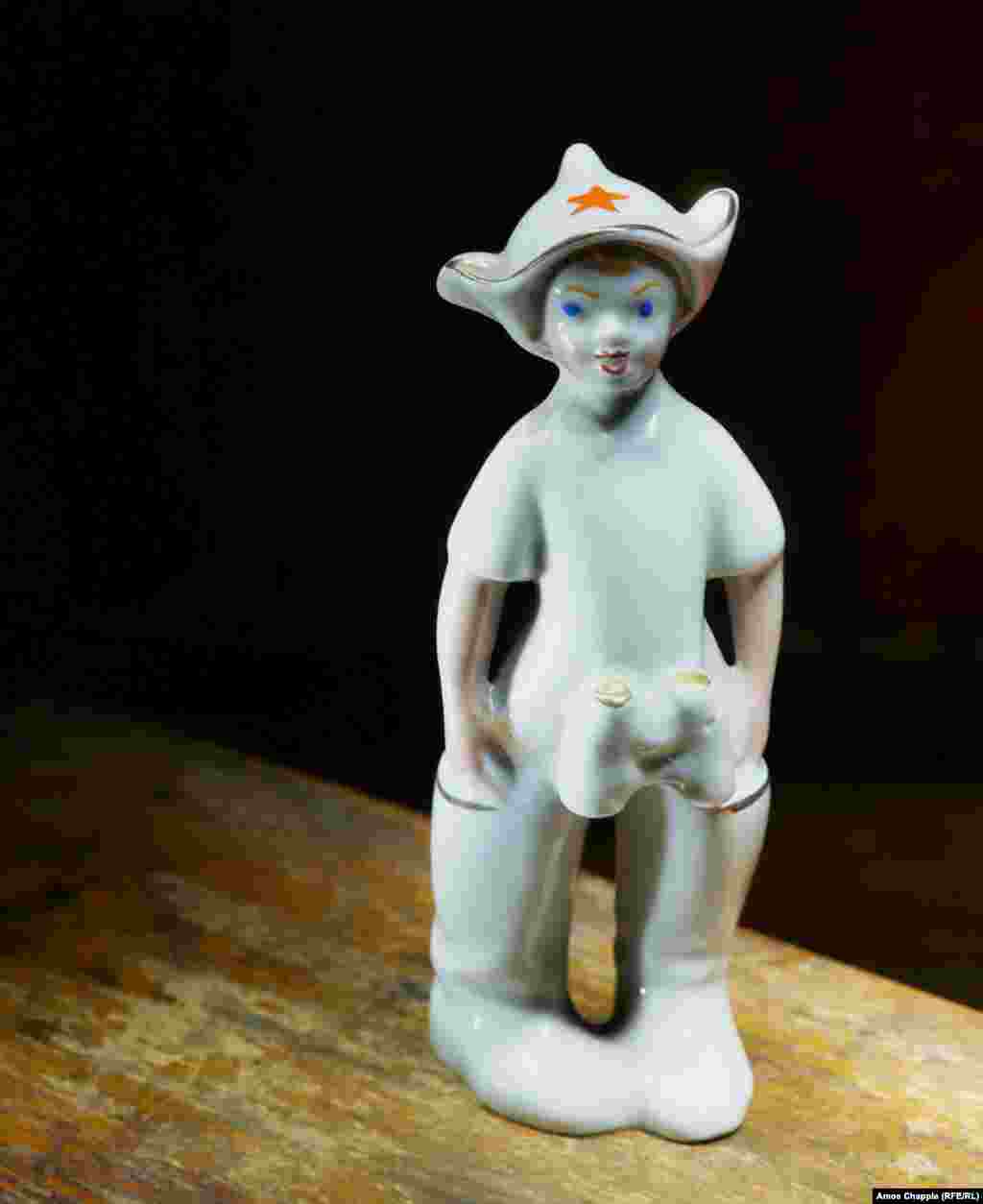 A porcelain figurine of a boy, presumably wearing his father&#39;s military boots and communist &quot;budyonovka&quot; cap.