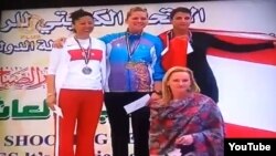 Kuweýtdäki halkara ýaryşynda nyşana ok atmakda birinji ýeri alan gazagystanly sportsmen Mariýa Dmitrienko (ortada) medal gowşurylyş dabarasynda Gazagystanyň milli gimniniň ýerine “Borat” kinokomediýasyndan parodiýa gimni diňlemeli boldy.