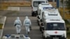 Medical specialists wearing protective gear walk past ambulances outside a hospital for patients infected with the coronavirus on the outskirts of Moscow.