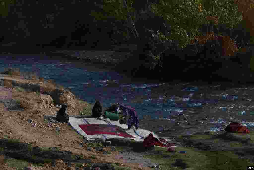 Women wash a carpet by one of the city&#39;s two rivers. د سیند پر غاړه ښځی قالین انځي په يو خار کی