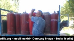 Мужчина берет баллон сжиженного газа. Иллюстративное фото.