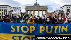 Участники акции с требованием не допустить войны держат плакаты и баннер у Бранденбургских ворот в столице Германии. 30 января 2022 года. 