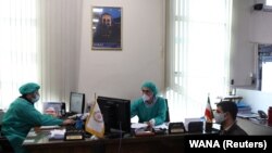 Angajații unei bănci din Teheran poartă măști chirurgicale și costum complet de protecție, 17 martie 2020