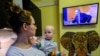 A woman holds her son as she watches a TV broadcast of Russian President Vladimir Putin's annual press conference in Moscow on December 14. 