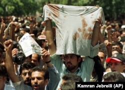 Ирандагы эскичилдердин режимине каршы студенттик нааразылык жыйынында коопсуздук кызматкерлери тарабынан токмоктолгон студенттин жеңсиз көйнөгүн көтөрүп чыгышты. Тегеран. 1999-жылдын 12-июлу.