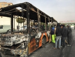 Жанармайдың қымбаттауына жаппай наразылық кезінде өртенген автобустың қаңқасына қарап тұрған адамдар. Исфахан, Иран, 17 қараша 2019 жыл.